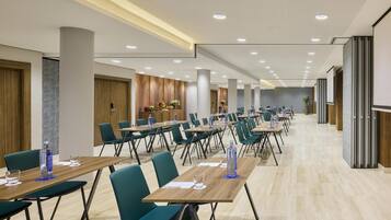 Un salón de conferencias con varias mesas y sillas, un techo con iluminación empotrada y una decoración en tonos neutros.