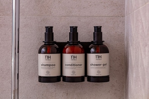 Trois flacons de produits d’accueil proposés par l’hôtel : shampoing, après-shampoing et gel douche, tous étiquetés avec les mentions « nh hotels » et « thé vert ».