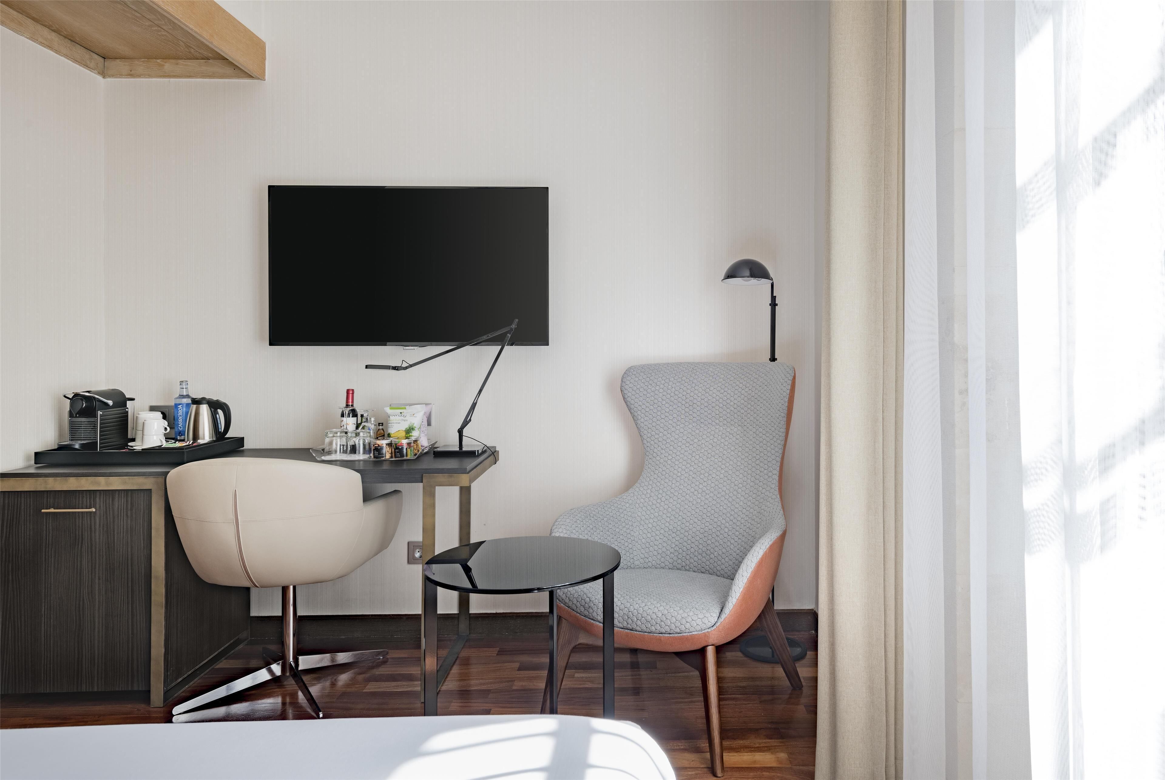 A modern room with a desk, two chairs, a flat-screen TV, and a lamp.