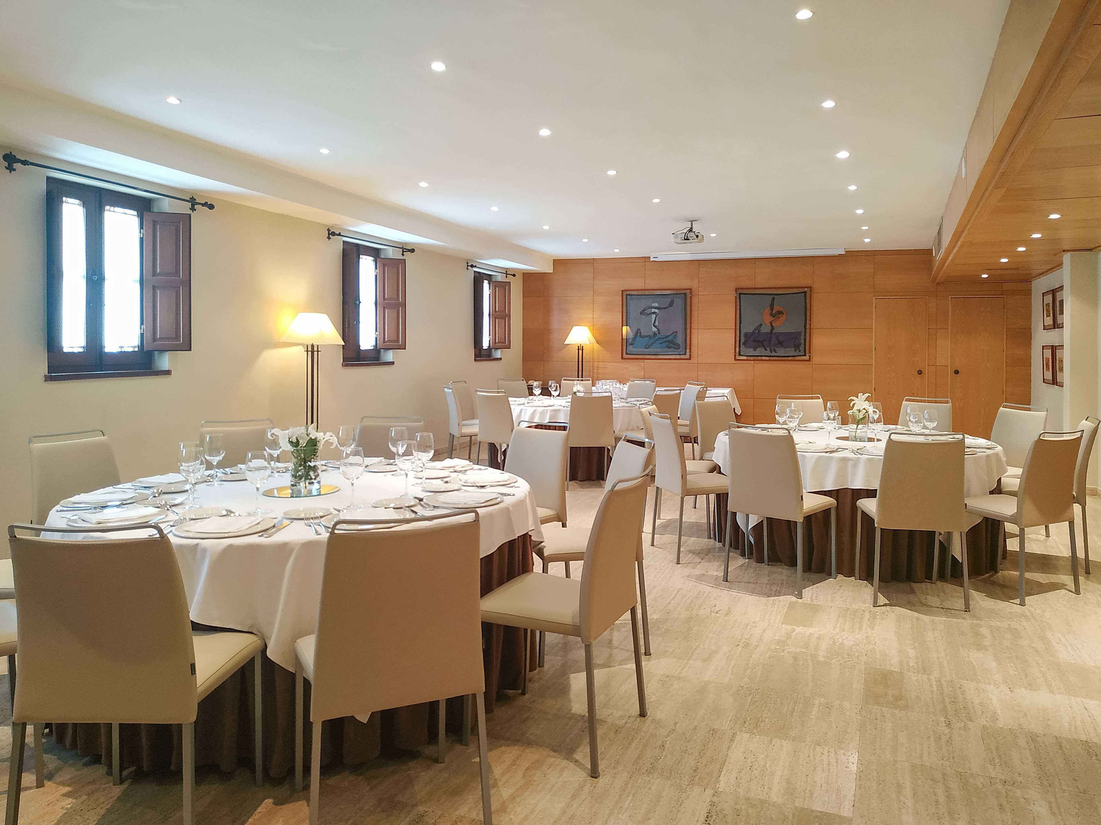 Un comedor con mesas redondas, sillas y una pared de madera decorada con obras de arte.