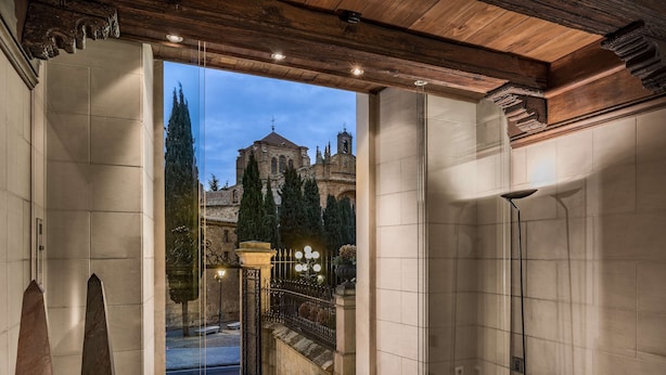 Amplia habitación con un ventanal grande que da a un edificio histórico y una escalera que conduce a un espacio exterior.