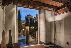 Amplia habitación con un ventanal grande que da a un edificio histórico y una escalera que conduce a un espacio exterior.