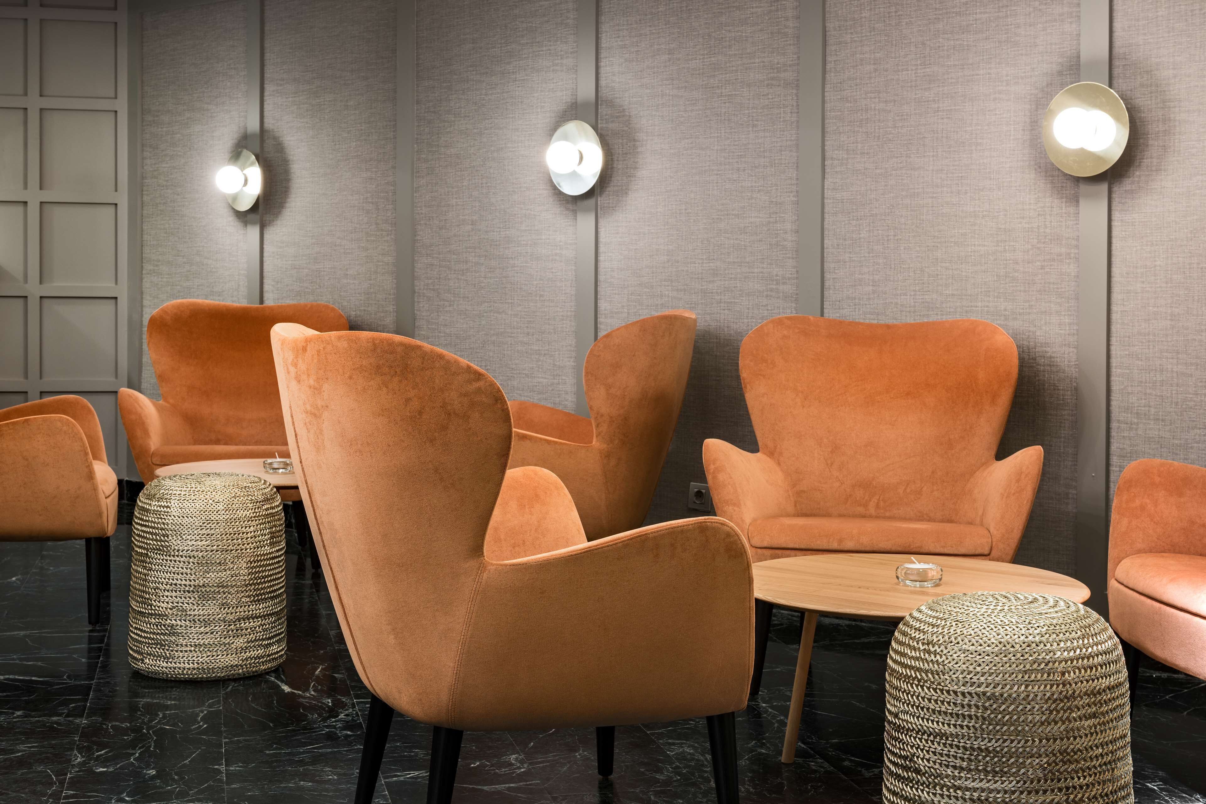 Un intérieur moderne avec des fauteuils orange moelleux, une table ronde en bois et des poufs en fibres naturelles posés sur un sol en marbre.