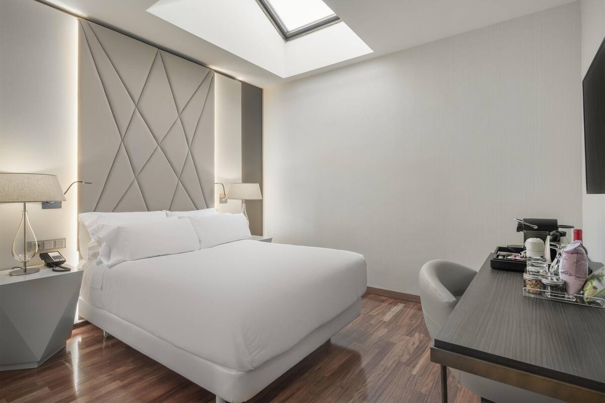Une chambre d’hôtel moderne équipée d’un lit, de tables de chevet, d’un bureau et d’une lucarne.