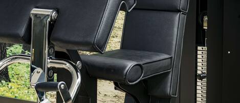 A row of black gym seats with metal frames and a metal handle, set against a backdrop of a forested area.