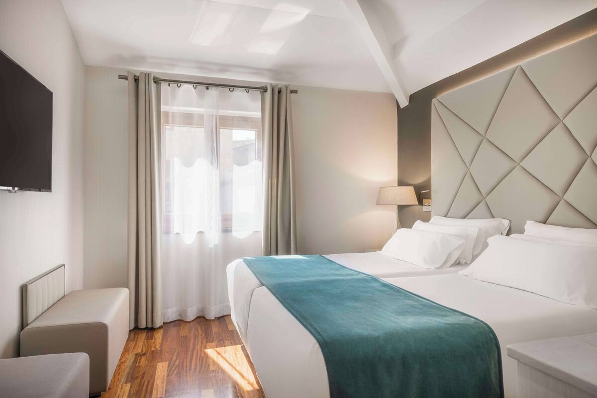 A hotel room with a bed, bedside table, and a TV mounted on the wall.