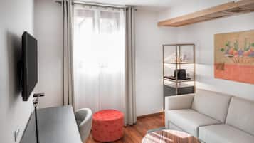 Una sala de estar moderna con un televisor de pantalla plana, un reposapiés rojo, un sofá blanco, una mesa de centro de vidrio y un cuadro en la pared.