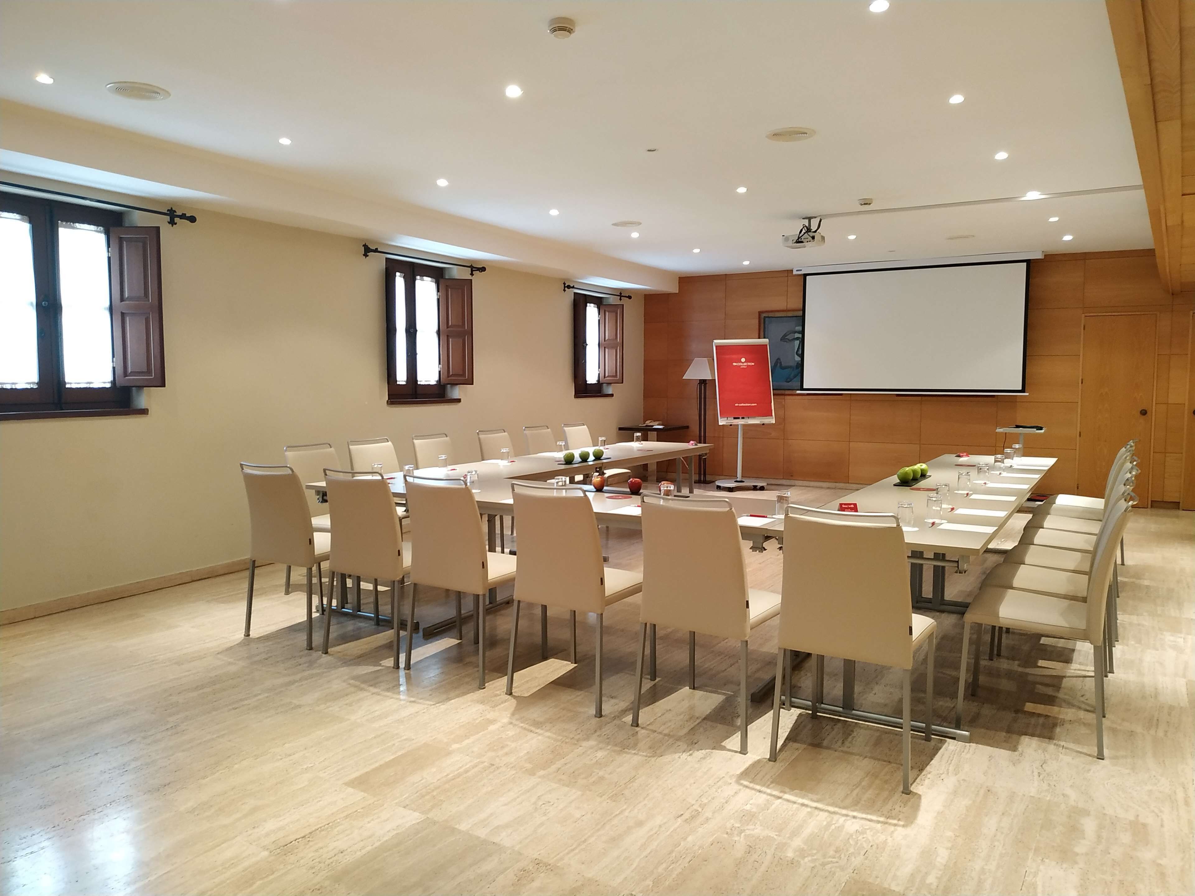 Una sala de conferencias con una larga mesa, sillas, una pantalla de proyector y una pizarra.