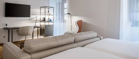 A modern hotel room with a large bed, a desk with a chair, a TV mounted on the wall, and a bookshelf.
