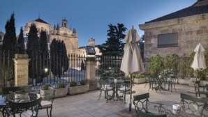 Un patio al aire libre con mesas y sillas, un edificio de piedra y una gran catedral al fondo.