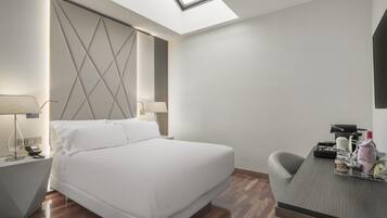 Habitación de hotel con cama, mesitas de noche, escritorio y tragaluz.