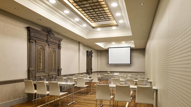A conference room with a large screen, wooden paneling, and rows of white chairs. - NH Collection Vigo (Vigo)