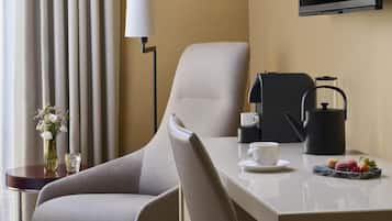Habitación de hotel con sofá, mesa de centro, televisor, lámpara y una mesita con una taza y aperitivos.