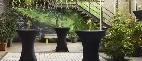 An outdoor seating area with black tables and chairs, a mural of a tree, and a staircase.