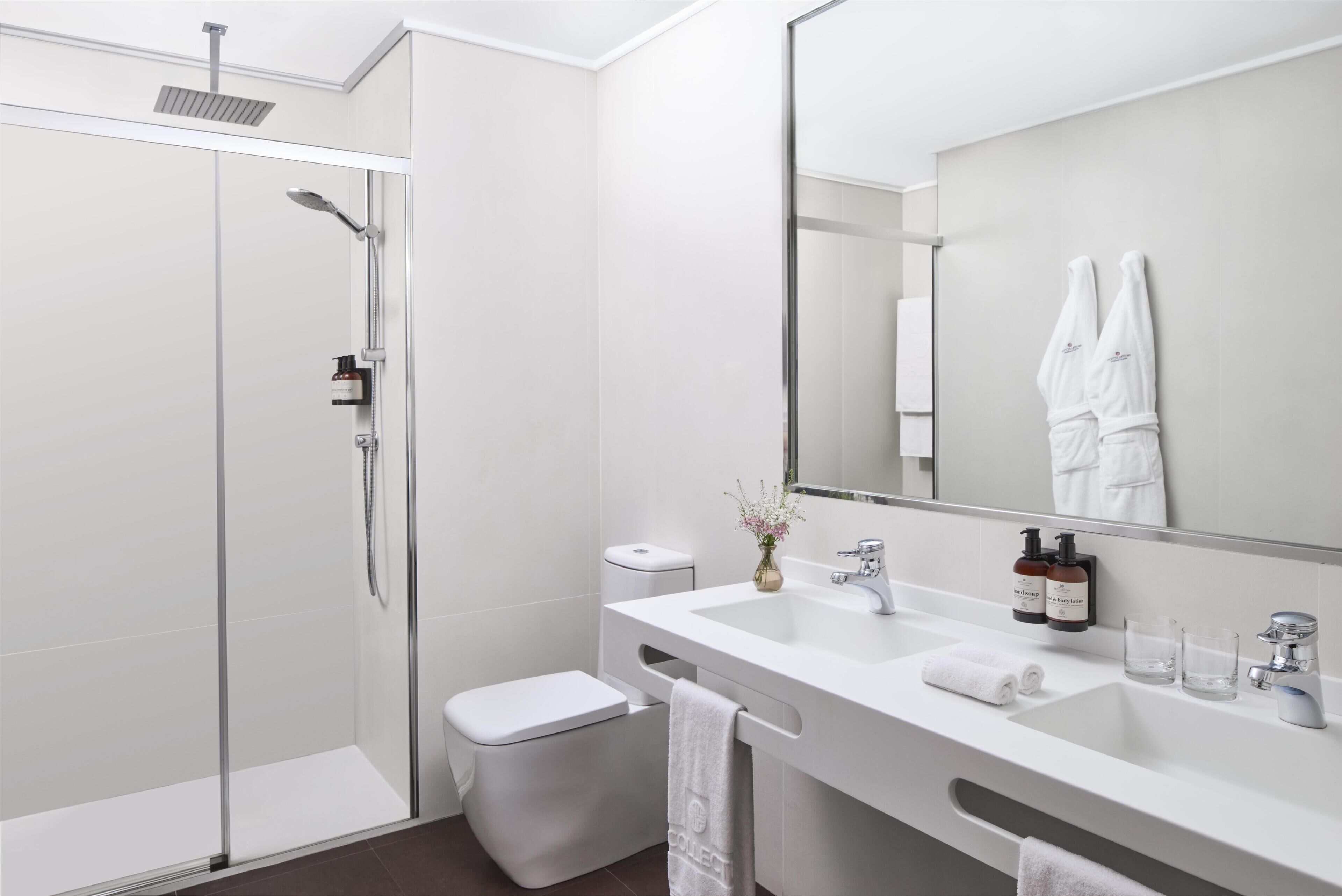 A modern bathroom with a glass-enclosed shower, a white toilet, a sink with a mirror, and two bottles of soap.