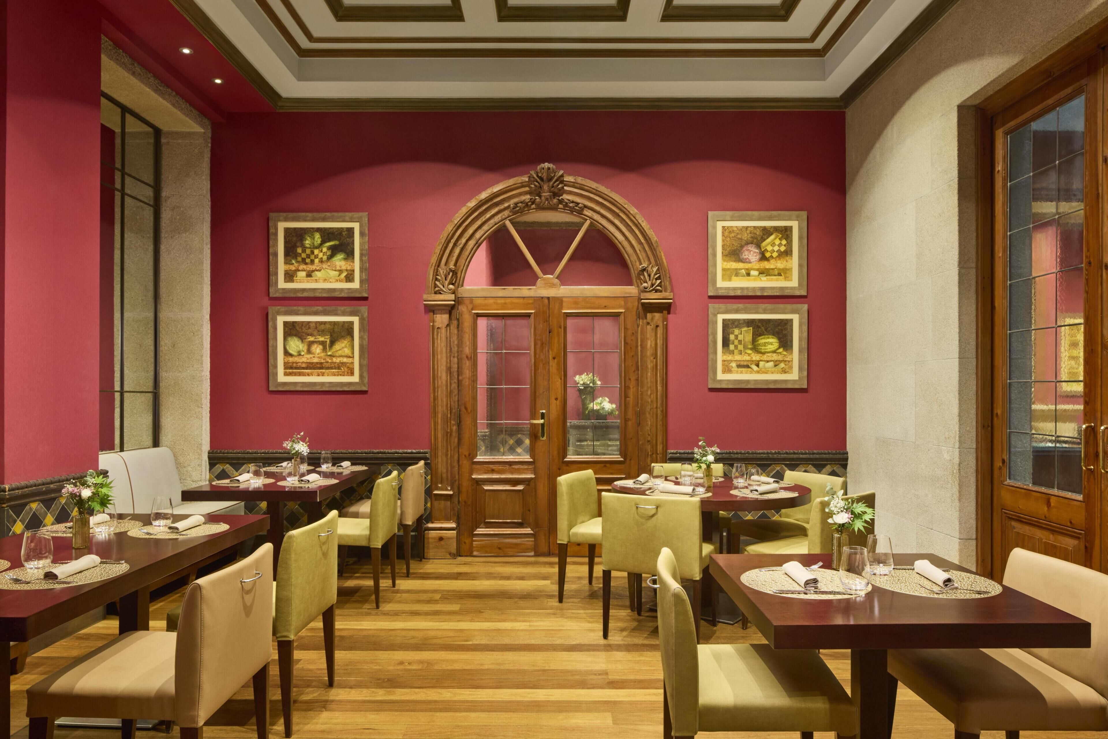 Un'area pranzo con diversi tavoli e sedie, una porta in legno con pannelli di vetro e opere d'arte appese alle pareti.