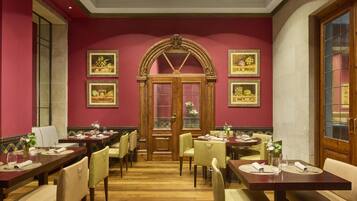 Un'area pranzo con diversi tavoli e sedie, una porta in legno con pannelli di vetro e opere d'arte appese alle pareti.