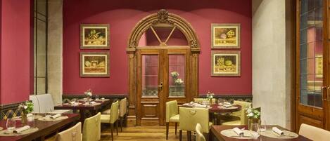 Un espace repas comprenant plusieurs tables et chaises, une porte en bois avec des panneaux de verre et des œuvres d’art encadrées accrochées aux murs.