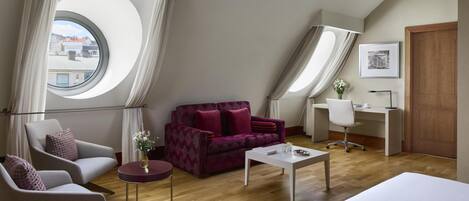 A modern loft bedroom with a large skylight, a sofa, a desk, and a chair.
