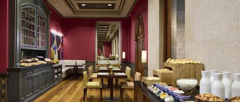 A hotel dining area with a long table, chairs, and buffet with various food items.