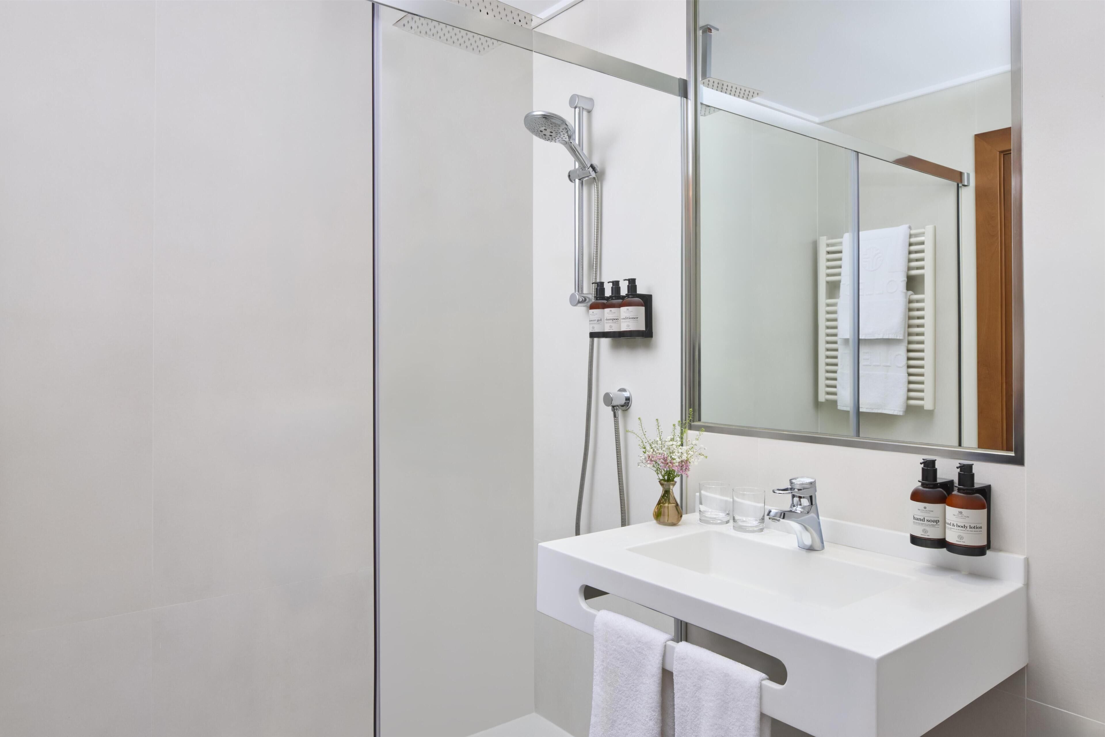 Un baño moderno con cabina de ducha de vidrio, un lavamanos blanco y un espejo que refleja un perchero.