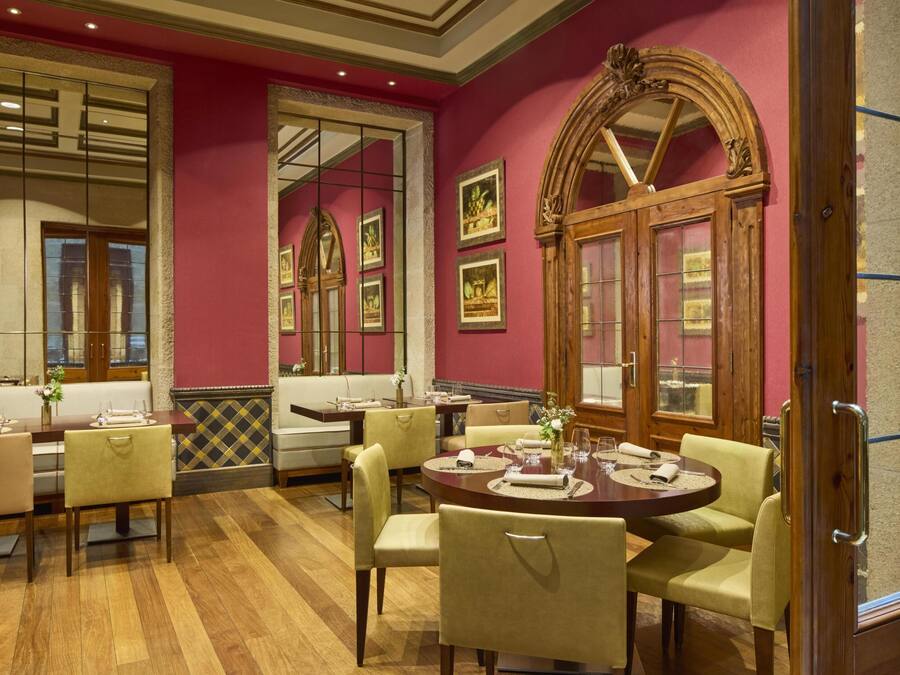 A dining area with tables and chairs, a wooden floor, and a red wall with framed pictures.