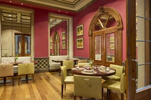 Un comedor con mesas y sillas, piso de madera y pared roja con cuadros enmarcados.