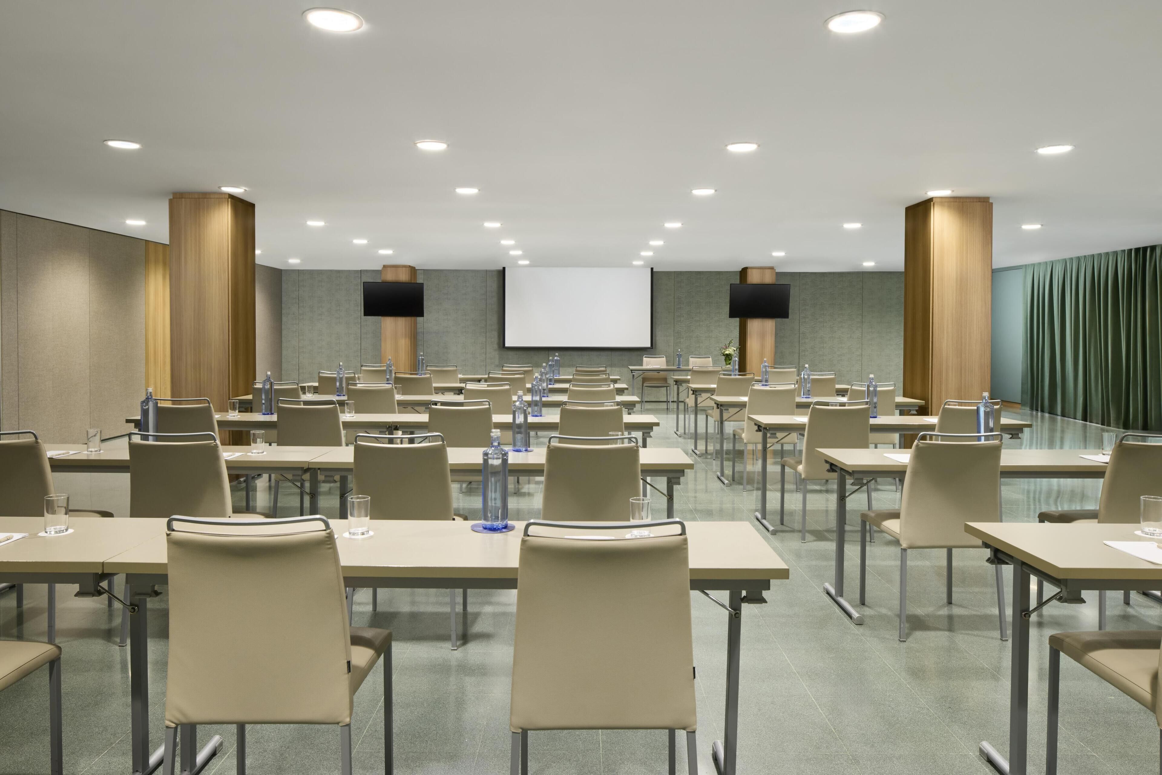A conference room with multiple tables and chairs, a large screen, and a projector.