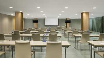 A conference room with multiple tables and chairs, a large screen, and a projector.