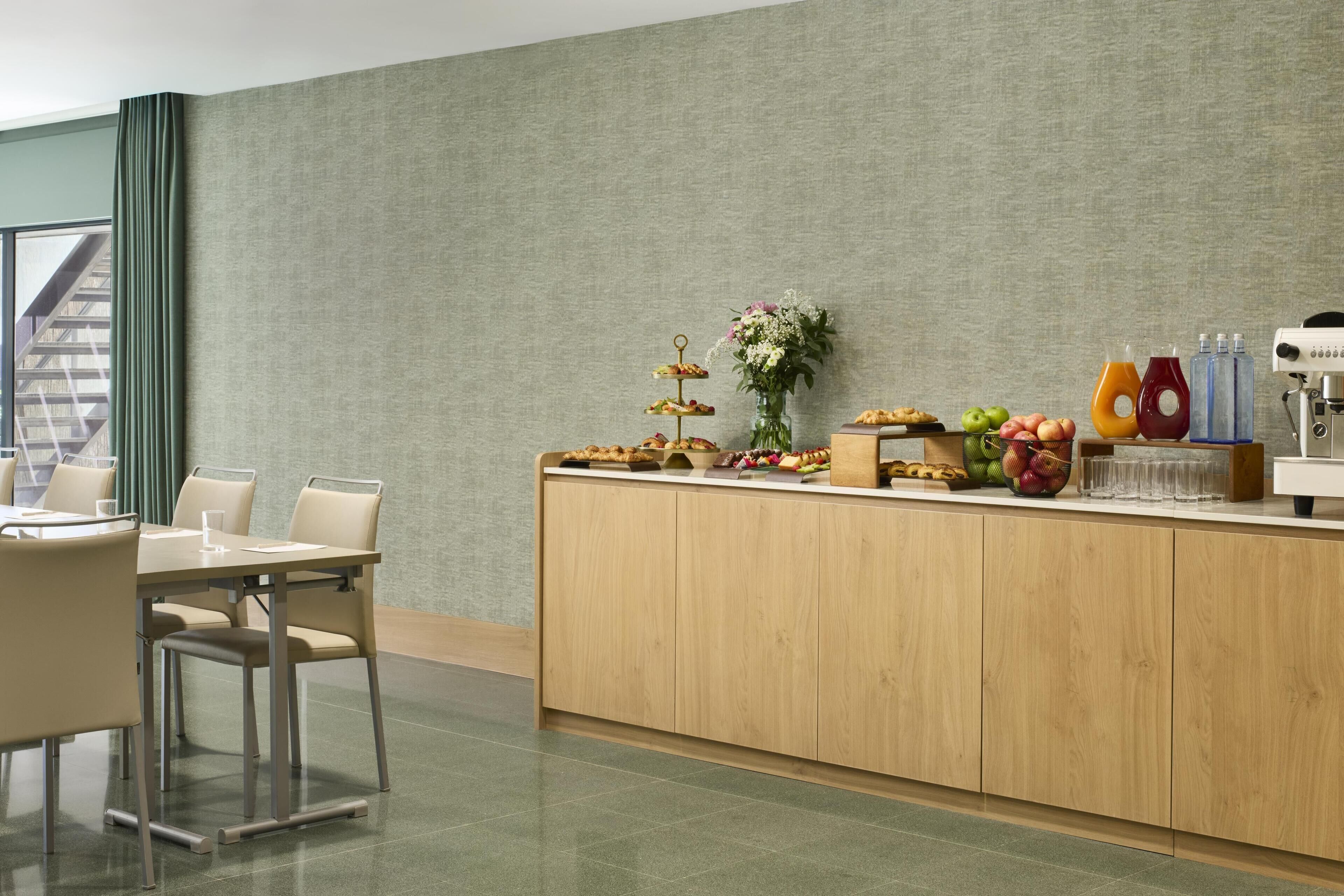 A hotel reception area with a wooden counter, a small flower arrangement, and various food items.