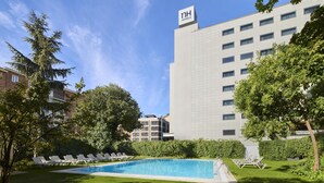 A hotel with a swimming pool, lounge chairs, and a large building with a sign. - NH Madrid Ventas (Madrid)