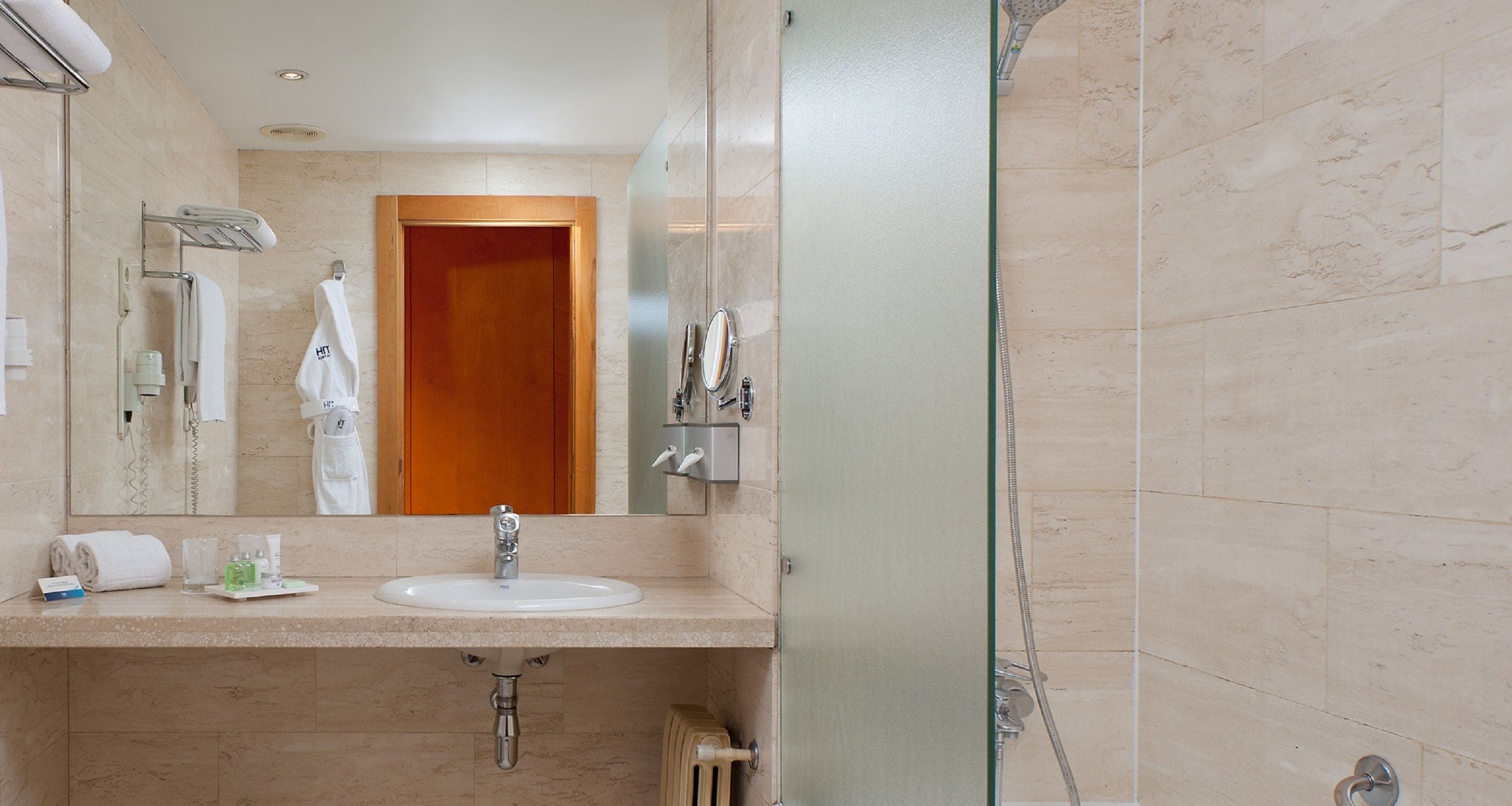Un baño de hotel con lavamanos, espejo, toallero y ducha.