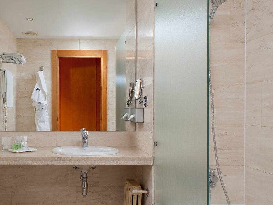 Un baño de hotel con lavamanos, espejo, toallero y ducha.