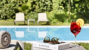 Une scène de bord de piscine avec un livre intitulé « KINFOLK » et un verre d’une boisson rouge agrémentée d’une tranche de citron.