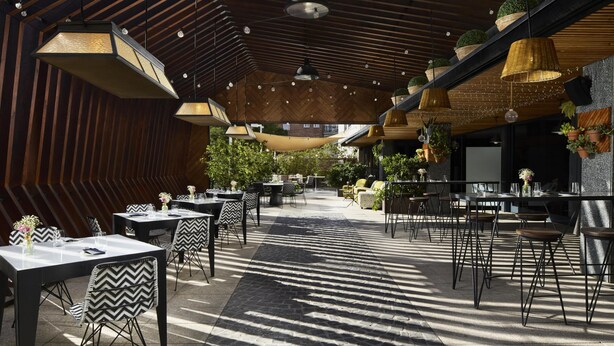 An outdoor dining area with tables and chairs, hanging plants, and a wooden ceiling structure. - NH Madrid Ventas (Madrid)