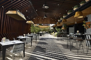 An outdoor dining area with tables and chairs, hanging plants, and a wooden ceiling structure. - NH Madrid Ventas (Madrid)
