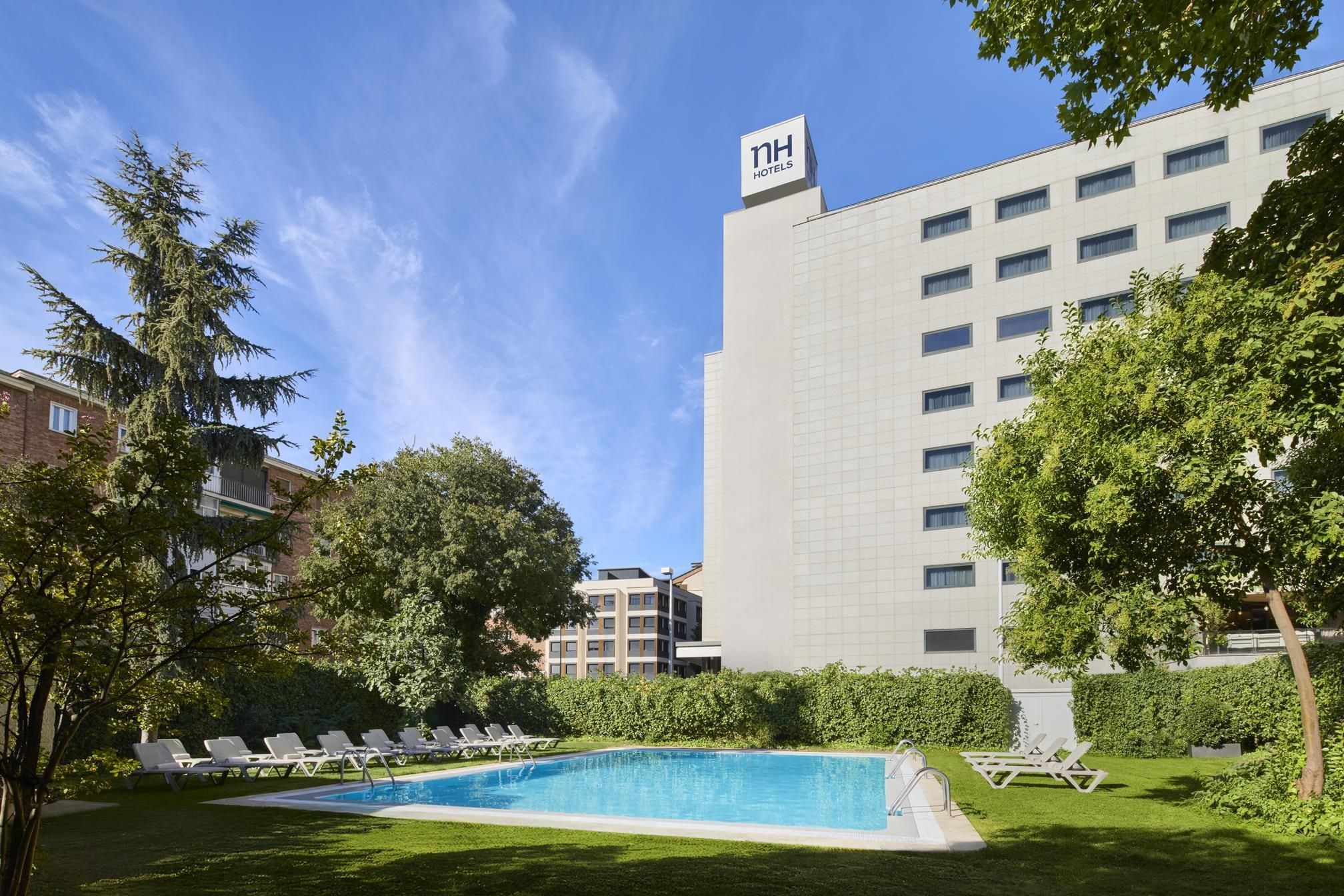 Un hotel con piscina, sillas de descanso y un edificio grande con un letrero.
