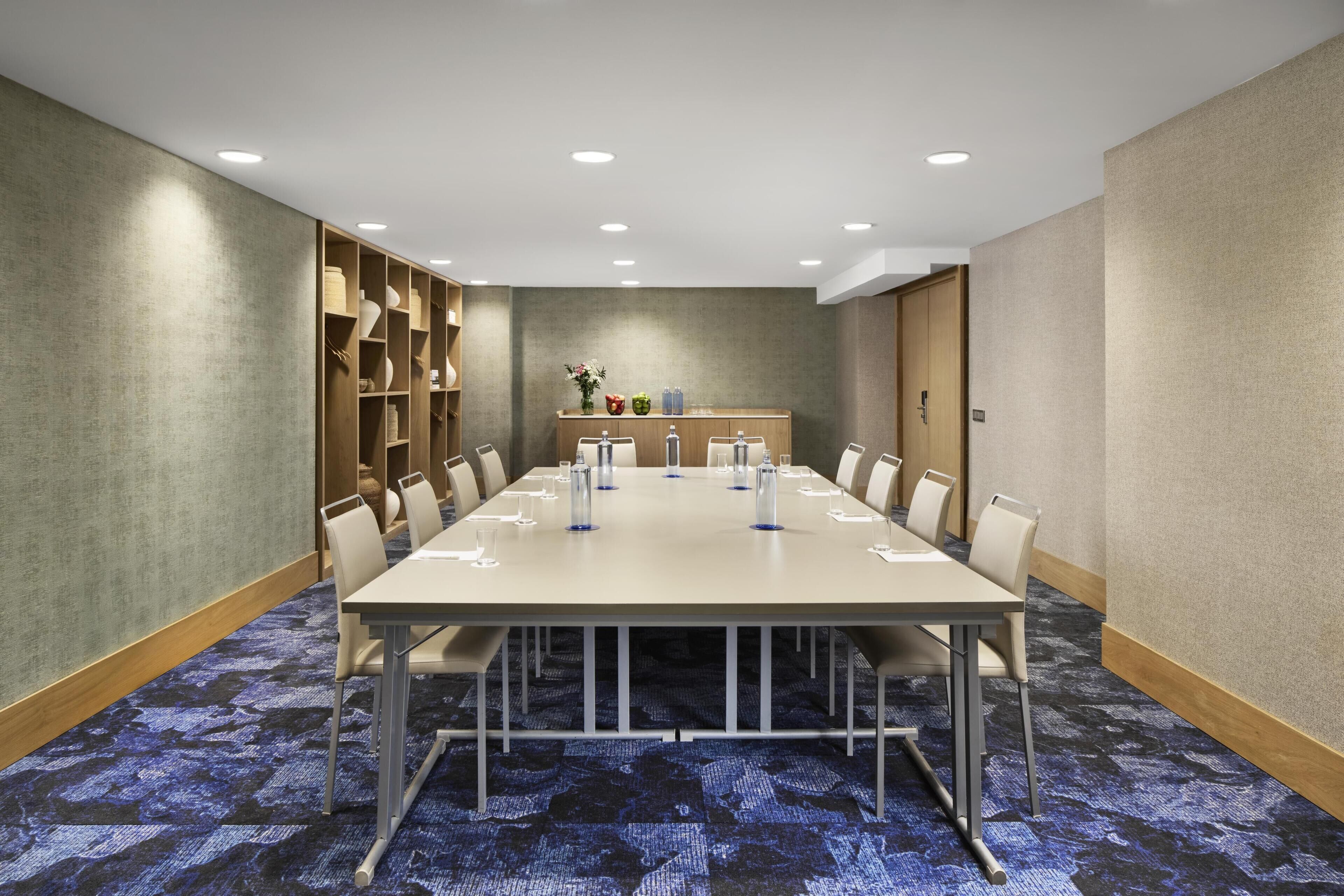 A conference room with a long table, chairs, and a small display area with items on shelves.