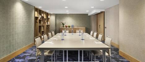 A conference room with a long table, chairs, and a small display area with items on shelves.