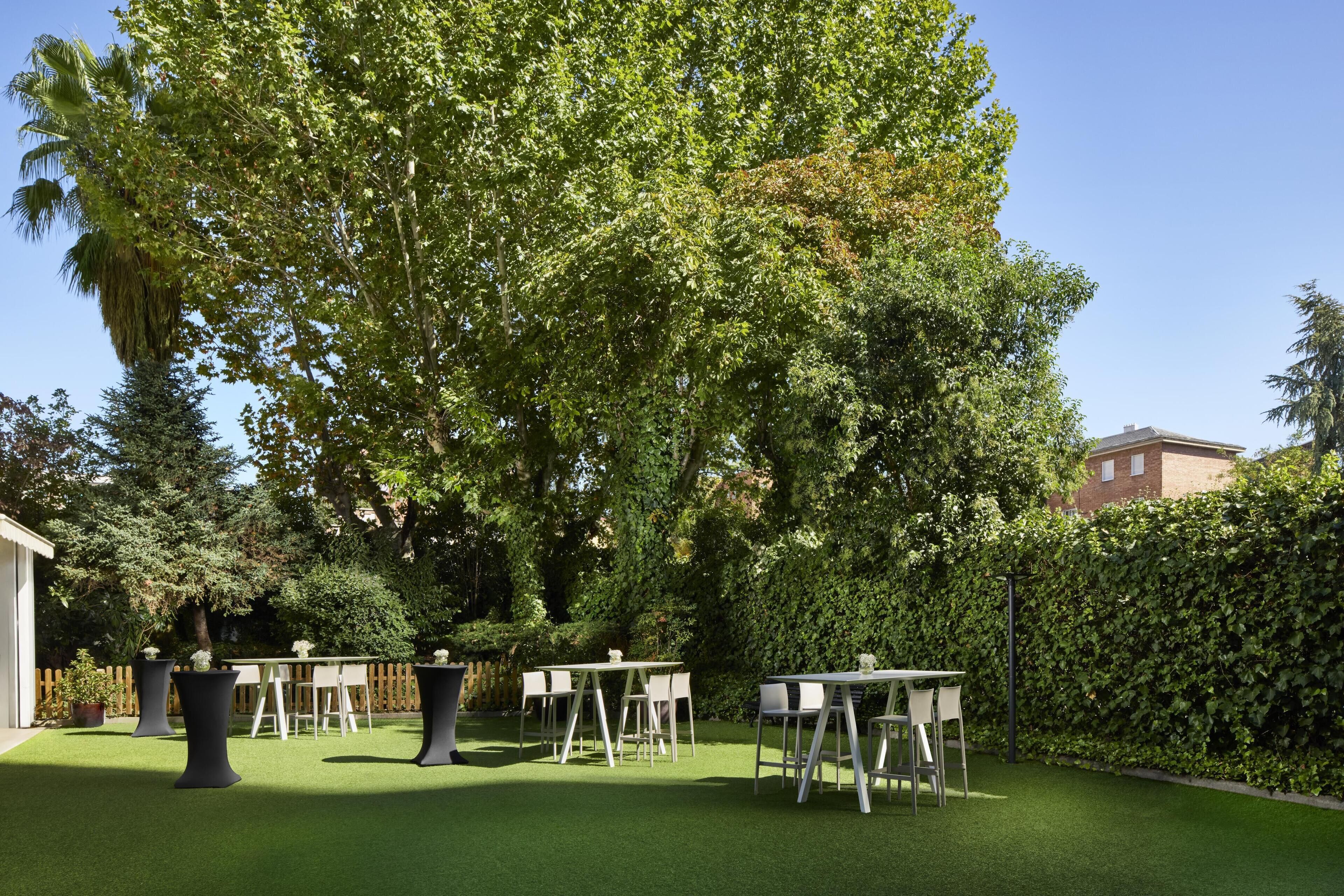 An outdoor patio area with tables and chairs, surrounded by lush greenery and trees.