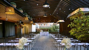 An indoor venue with rows of chairs and tables, a stone-tiled floor, hanging lights, and potted plants. - NH Madrid Ventas (Madrid)