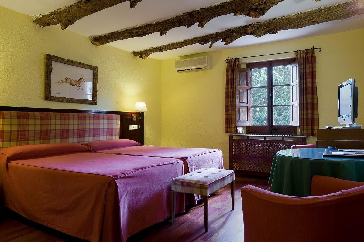 Ein Zimmer mit zwei Betten, einem Tisch und einem fensterverzierten Fenster.