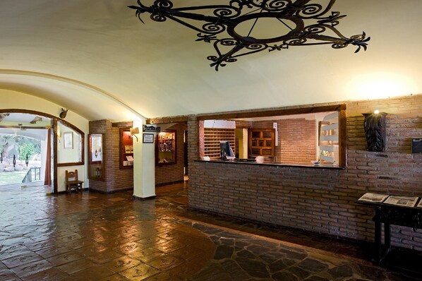 A lobby with a brick wall, a wooden bench, and a reception desk. - La Perdiz (La Carolina)