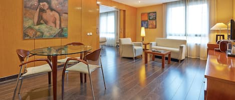 Una habitación de hotel moderna con una mesa de comedor de vidrio, asientos cómodos, un sofá y obras de arte en las paredes.