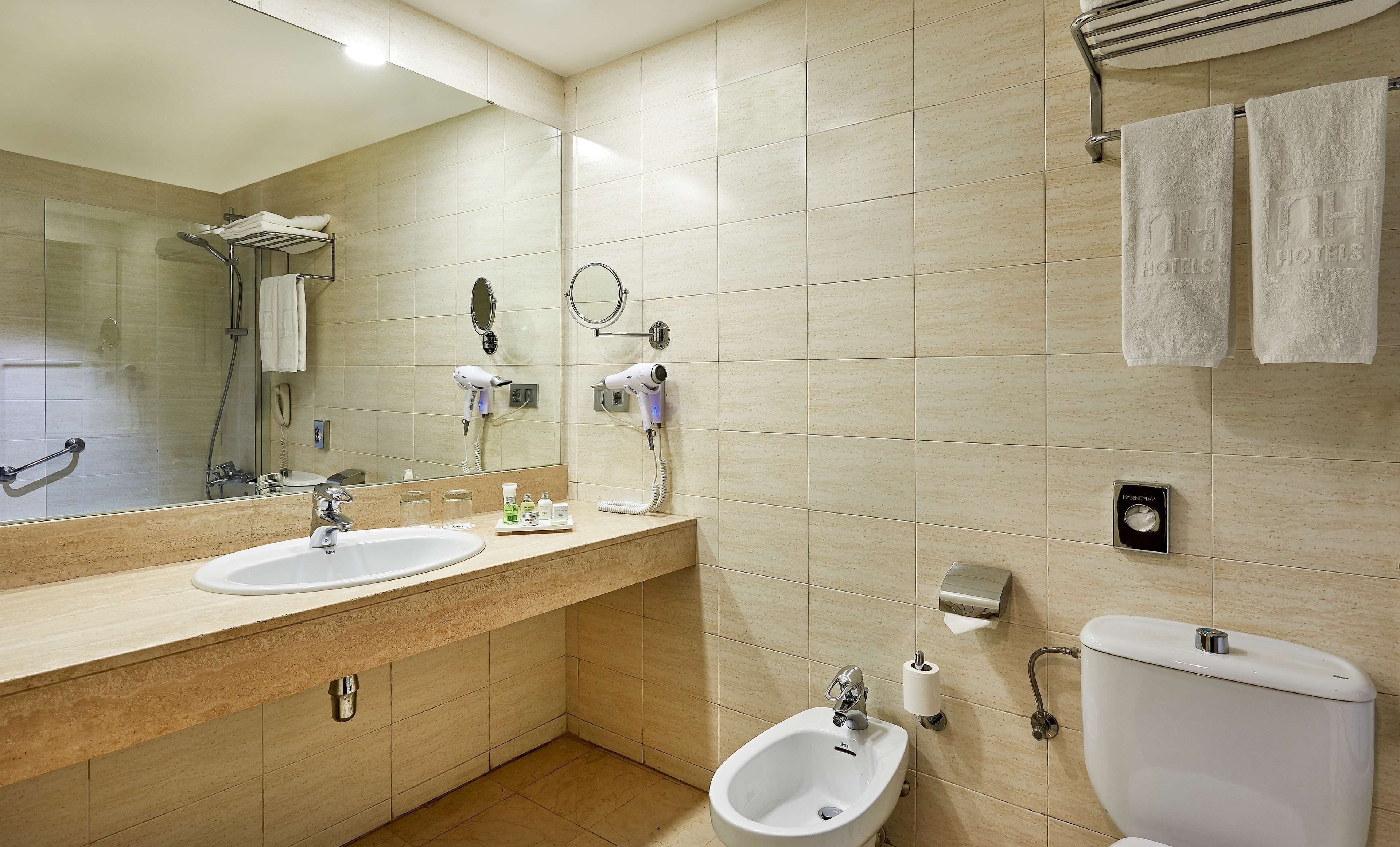 A modern bathroom with two sinks, a bidet, a toilet, a hairdryer, and a towel rack.