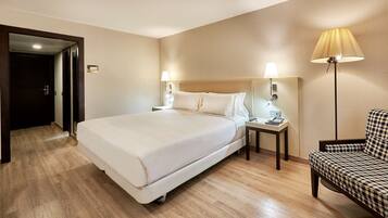 A hotel room with a large bed, bedside lamps, a small table with a phone and remote, and a patterned armchair.