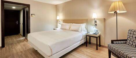 A hotel room with a large bed, bedside lamps, a small table with a phone and remote, and a patterned armchair.