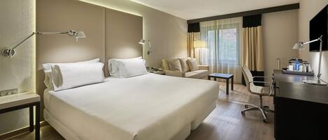 A hotel room with a large bed, a desk, a chair, and a sofa.