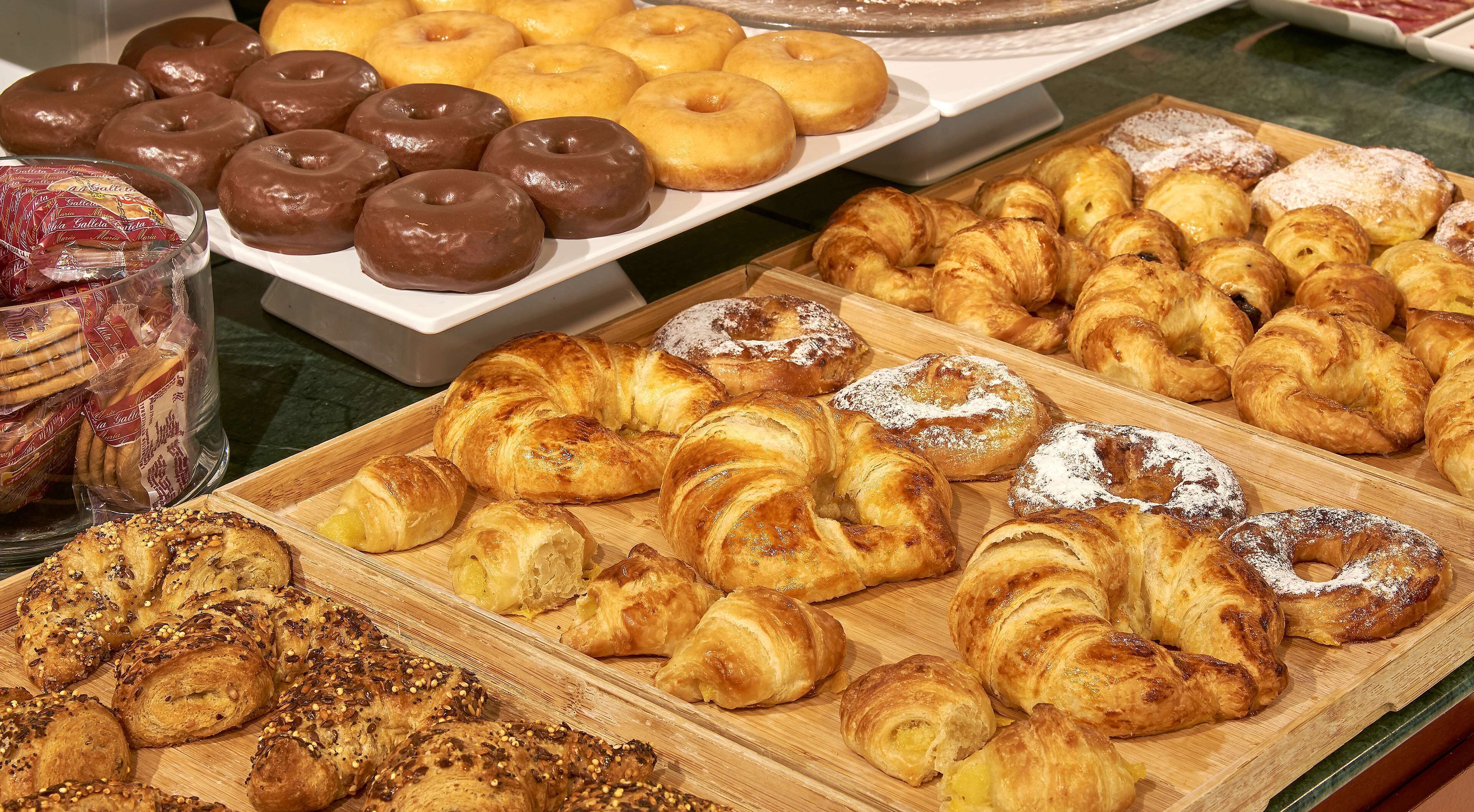 Verschiedene Backwaren, darunter schokoladenüberzogene Donuts, Croissants und weitere Gebäcke, präsentiert auf Holzbrettern.