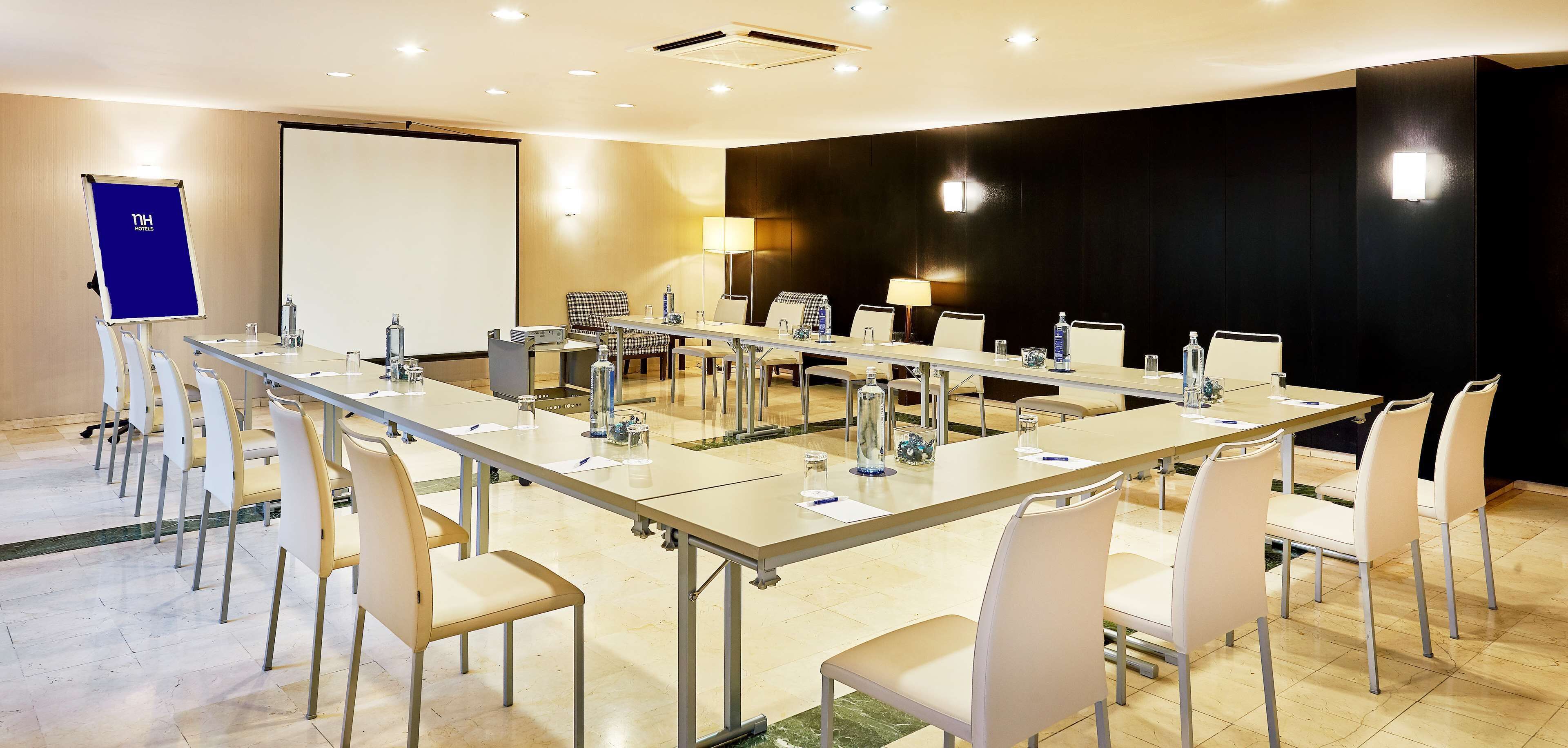 A conference room with a long table, white chairs, a projector screen, and a black accent wall.